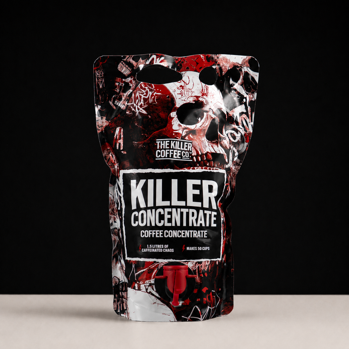 A stand-up pouch of The Killer Coffee Co. Killer Concentrate coffee concentrate, featuring a black, white, and red skull graphic design with a red spout, set against a black background and light beige surface.